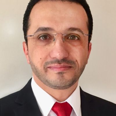 a head and shoulders shot of Rafid Al-Khannak wearing a black suit with a red tie wearing glasses and looking into the camera face on